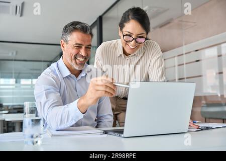 Happy diverse professional employees working in office using laptop, talking. Stock Photo