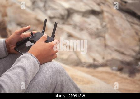 Close-up of man holding drone remote controller while sitting on rock Stock Photo