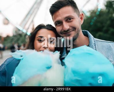 Portrait of a young couple looking at the camera holding a blue cotton candy Stock Photo