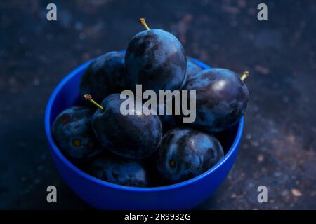 Ripe juicy plums in a bowl on a table. Summer fruits. Stock Photo