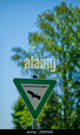 triangular green-white sign lettering 'Landschaftsschutzgebiet' (German for landscape conservation area) in front of a green tree and a clear blue sky Stock Photo