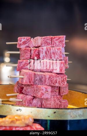 the closeup image of A5 wagyu beef stick on sale from food stall in Tsukiji Outer Market Tokyo Japan. It is Japan’s “Food Town,” where one can encount Stock Photo