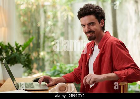 Portrait of smiling solopreneur working on laptop at his office desk and smiling at camera Stock Photo