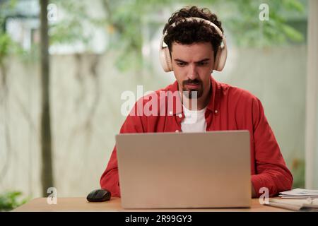 Concetrated programmer wearing headphones when working on laptop at home Stock Photo