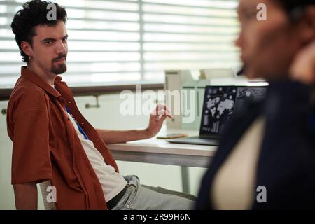 Smiling manager leaning back in his chair and offering coworker to go for coffee break Stock Photo