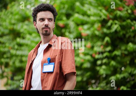 Smiling software developer with badge on shirt standing outdoors and looking away Stock Photo