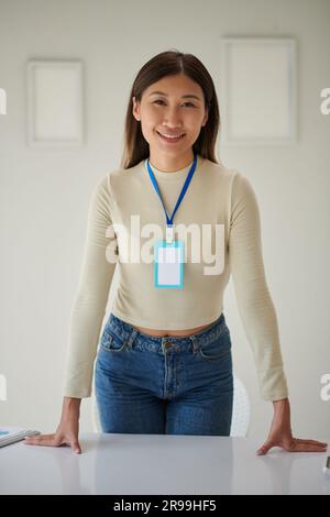 Portrait of company manager with empty badge leaning on office desk and smiling at camera Stock Photo
