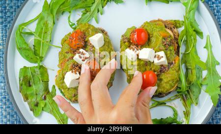 Chef woman hand put a cherry tomato on avocado toast Stock Photo