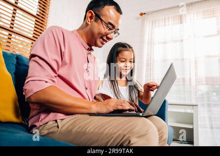 Father using laptop playing with daughter in living room Stock Photo