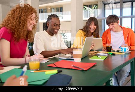 Smiling young people doing homework using laptop tablet in college campus cafeteria. Generation z. Stock Photo