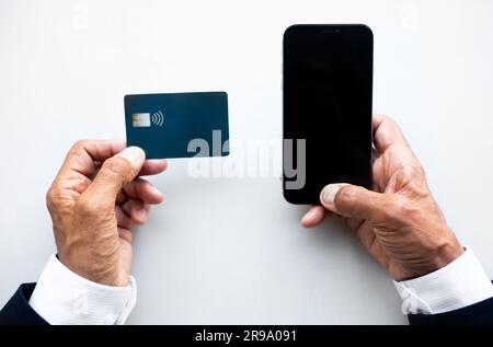 Mature european man in uses credit card and smartphone with empty screen on white table, top view Stock Photo