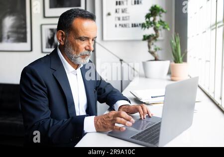 Serious concentrated mature european man in suit working on laptop in modern office interior Stock Photo