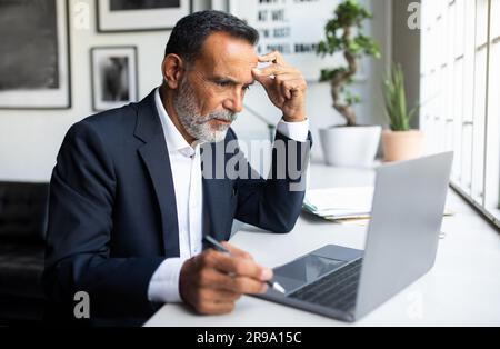 Sad serious concentrated mature european man in suit working on laptop, creating solution in office Stock Photo