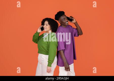 Positive multicultural lovers standing back to back, talking on phones Stock Photo