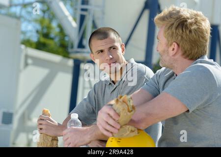 two male construction workers eating sandwiches for lunch Stock Photo