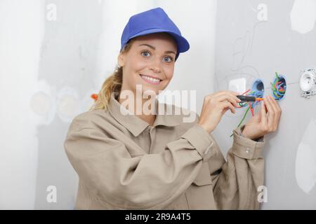 smiling female electrician installing a wall socket Stock Photo