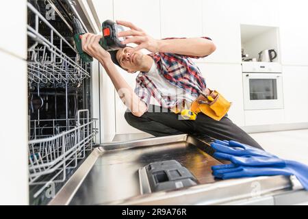 Worker using screwdriver to repair dishwasher at home stock photo Stock Photo