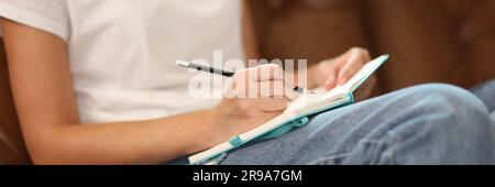 Woman sitting on sofa and writing something on notepad Stock Photo