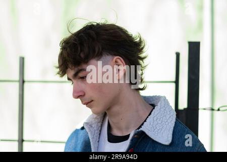 Side profile of a handsome young man wearing a denim jacket and leaning against a metal fence Stock Photo