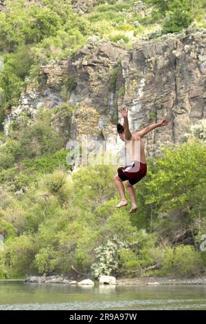 A young man is jumping off a cliff into the water below in Twin Falls, Idaho. Stock Photo
