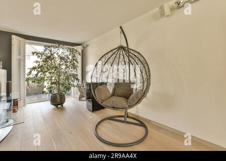 a living room with a hanging chair in the middle and a tv on the right side, next to an open door Stock Photo