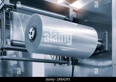 Automatic industrial machine for plastic packaging with light effect of products and food. shaft of an automated packaging line with plastic film in a Stock Photo