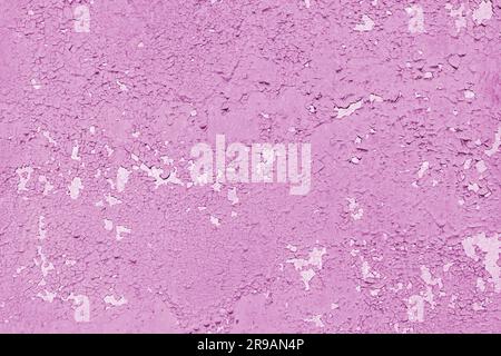 Concrete wall with old cracked, peeling flaking pink paint. Weathered rough painted surface with patterns of cracks and peeling, grunge, aged texture. Stock Photo