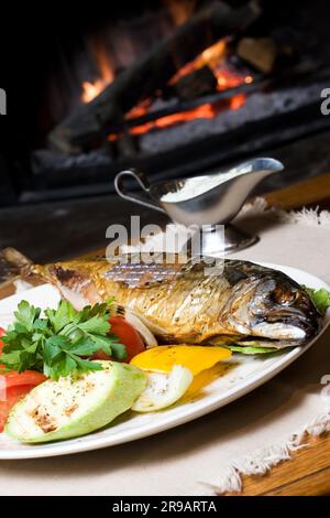 A fish dinner on a plate with vegetables in front of a fire Stock Photo