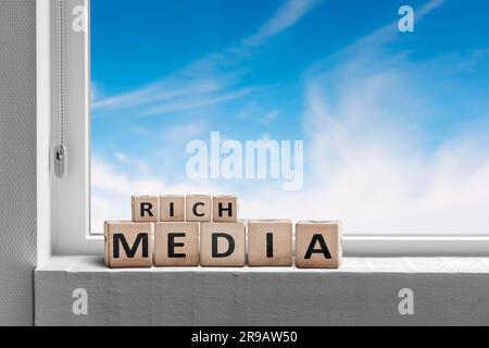 Rich media sign written on wooden blocks in a window with a blue sky outside Stock Photo