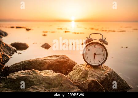 Alarm clock on a rock in the sunrise by the ocean in the morning Stock Photo