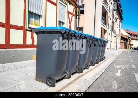 Eight garbage cans on the street outside an old house in the summer Stock Photo