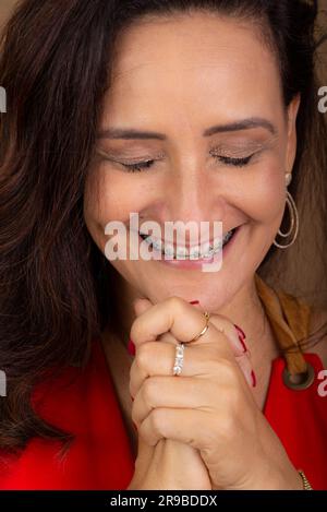 Mature woman, very happy, holding both hands close to her face. Passionate and hopeful person. Isolated on brown background. Stock Photo