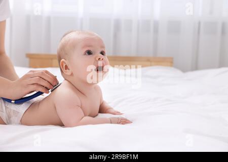 Pediatrician examining cute little baby with stethoscope in clinic, closeup. Space for text Stock Photo