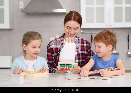 Happy mother and children playing with different math game kits at white marble table in kitchen. Study mathematics with pleasure Stock Photo