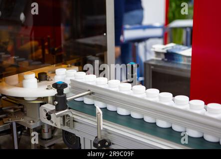 White plastic bottle on capsule filling machine conveyor belt in production line. Pharmaceutical industry Stock Photo