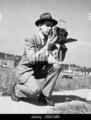 United States:   c. 1936 A press photographer aims his camera. Stock Photo