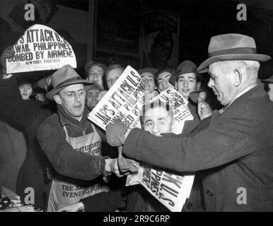 New York, New York:  December 7, 1941 Shocked and angry crowds in Times Square grab New York Enquirer newspapers bearing the headlines of Japan's attack on the U.S. held Phillipines and Pearl Harbor in Hawii. Stock Photo