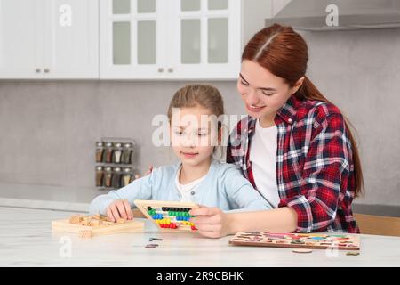 Happy mother and daughter playing with different math game kits at white marble table in kitchen. Study mathematics with pleasure Stock Photo