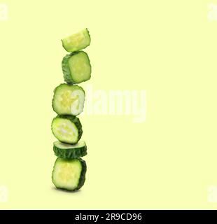 Stack of fresh cucumber pieces on pale light yellow green background, space for text Stock Photo