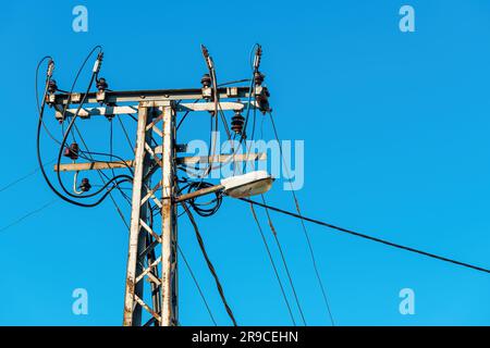 Old power utility and street light pole with cables and wires against blue sky Stock Photo