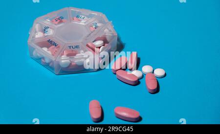 Organizer weekly shots on blue background with Copy space for your text. Closeup of medical pill box with doses of tablets for daily take medicine with white pink drugs and capsules. Daily vitamins at home. Medication dietary supplements, immunity and disease prevention Fish oil softgel, vitamin D and C omega minerals, fiber, fatty amino acids, probiotics sedatives. Health care and diseases cure Stock Photo