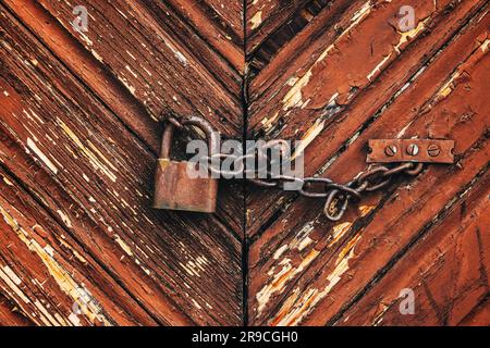 Old rusty corroded padlock with chain on wooden farm barn door as background Stock Photo