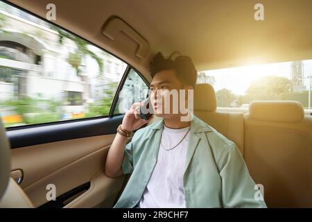 Young Vietnamese man talking on phone when riding taxi car to work Stock Photo