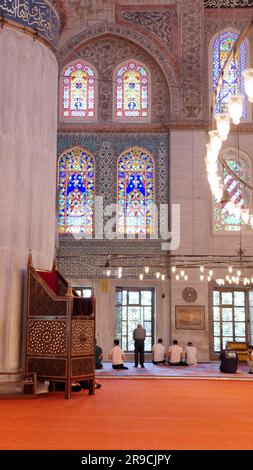 Men praying inside the Sultan Ahmed Mosque aka The Blue Mosque Istanbul, Turkey. Wooden minbar aka pulpit left Stock Photo
