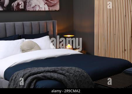 Lamp, ottoman and comfortable bed with cushions in room. Stylish interior Stock Photo