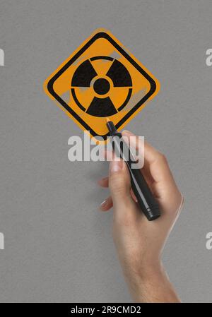 Man painting radiation warning symbol with marker on light grey surface, closeup Stock Photo