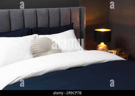 Comfortable bed with cushions, lamp and different decor on bedside table in room. Stylish interior Stock Photo