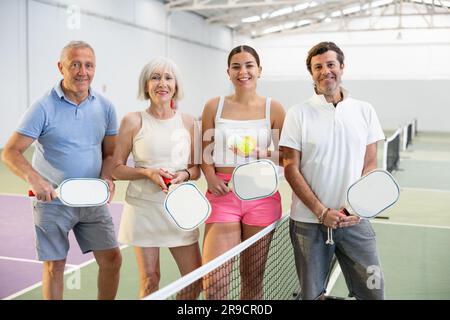 Group of happy smiling men and women of different ages in sportswear with rackets and balls in hands posing near net Stock Photo