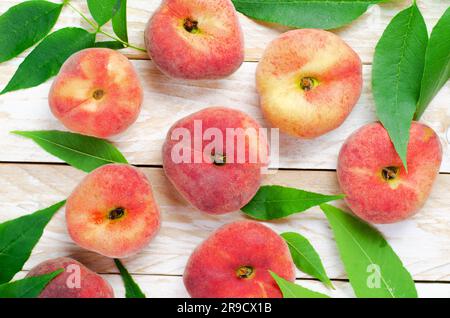 Fresh Flat Peaches, Chinese Saturn Donut Peaches with Leaves on Bright Background Stock Photo
