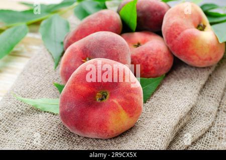 Fresh Flat Peaches, Chinese Saturn Donut Peaches with Leaves on Bright Background Stock Photo